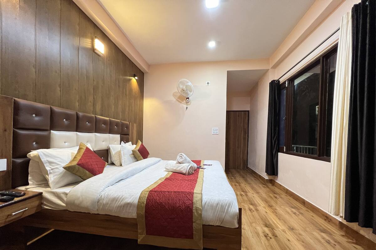Habitación de hotel con una cama grande, cabecera de madera y una ventana con cortinas.