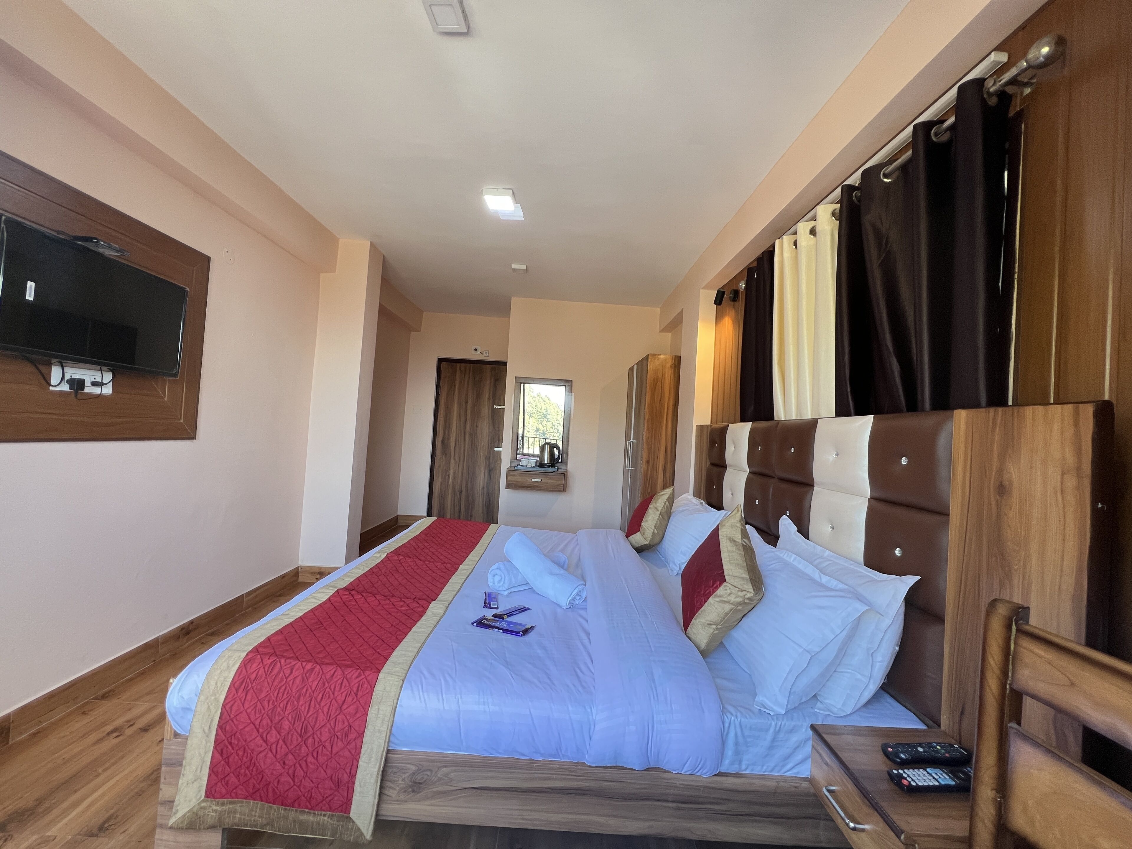 A hotel room with a large bed, a TV mounted on the wall, and a wooden headboard.