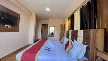 A hotel room with a large bed, a TV mounted on the wall, and a wooden headboard.