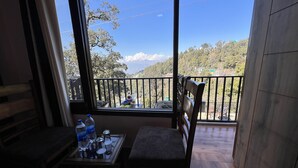 Un balcón con vista a un paisaje montañoso, una mesa con botellas de agua y una silla.