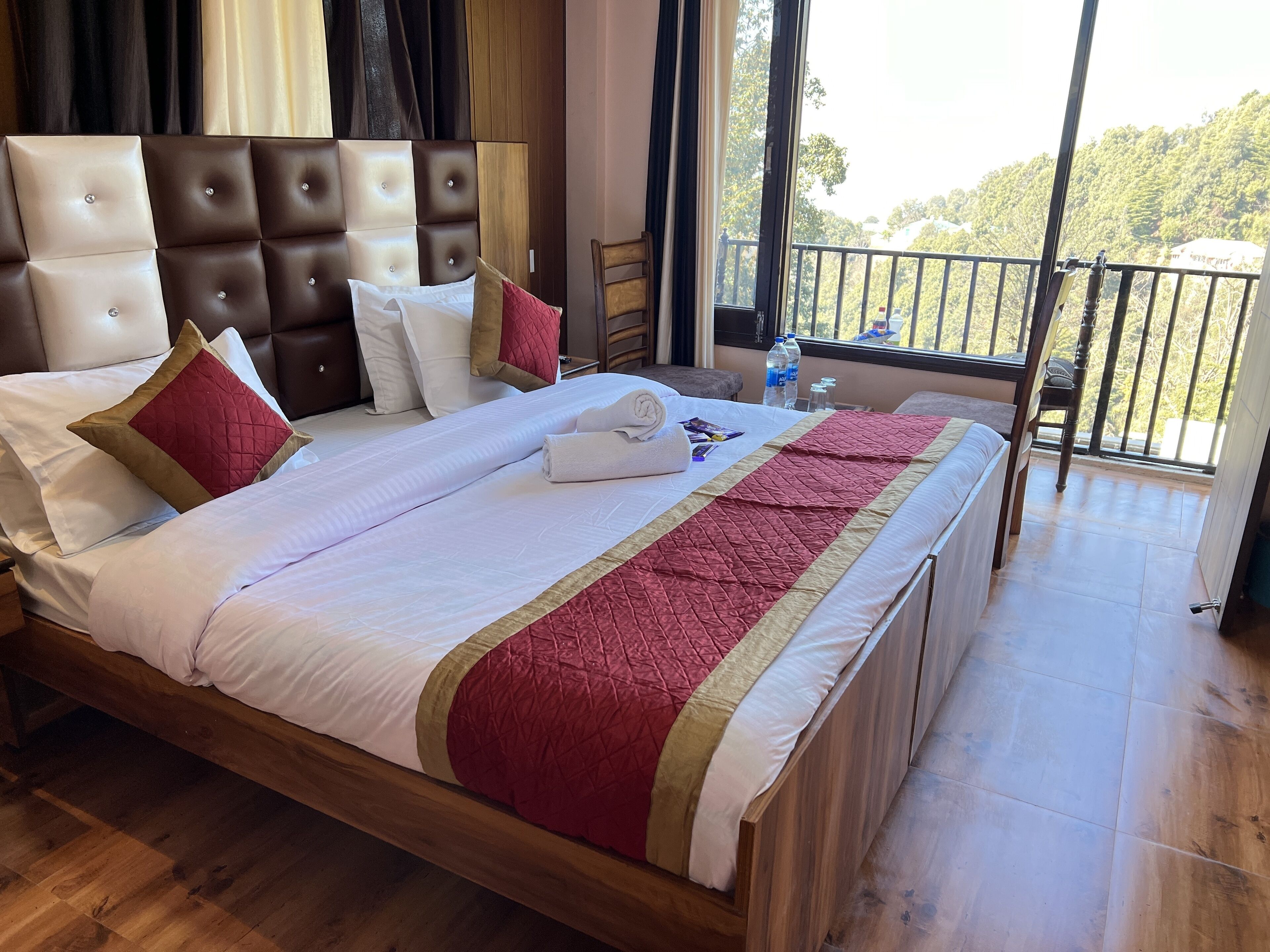 Una habitación de hotel con una cama grande, cabecera de madera y un balcón con vistas a árboles.