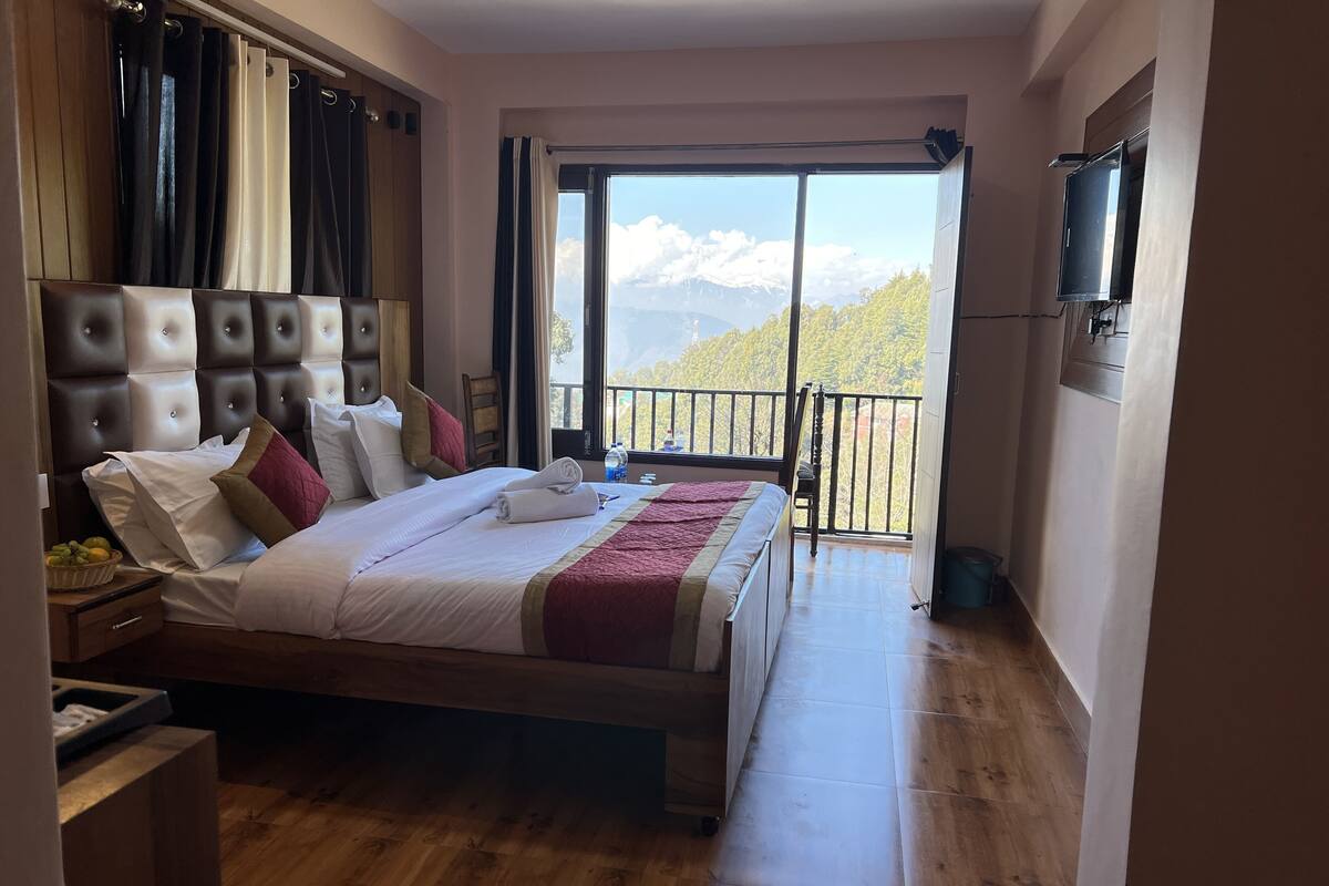 Habitación de hotel con una cama grande, piso de madera, balcón con vistas a las montañas y televisor montado en la pared.