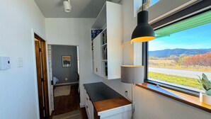 A modern kitchen with a built-in island, white cabinetry, and a view of a road and hills through a large window.