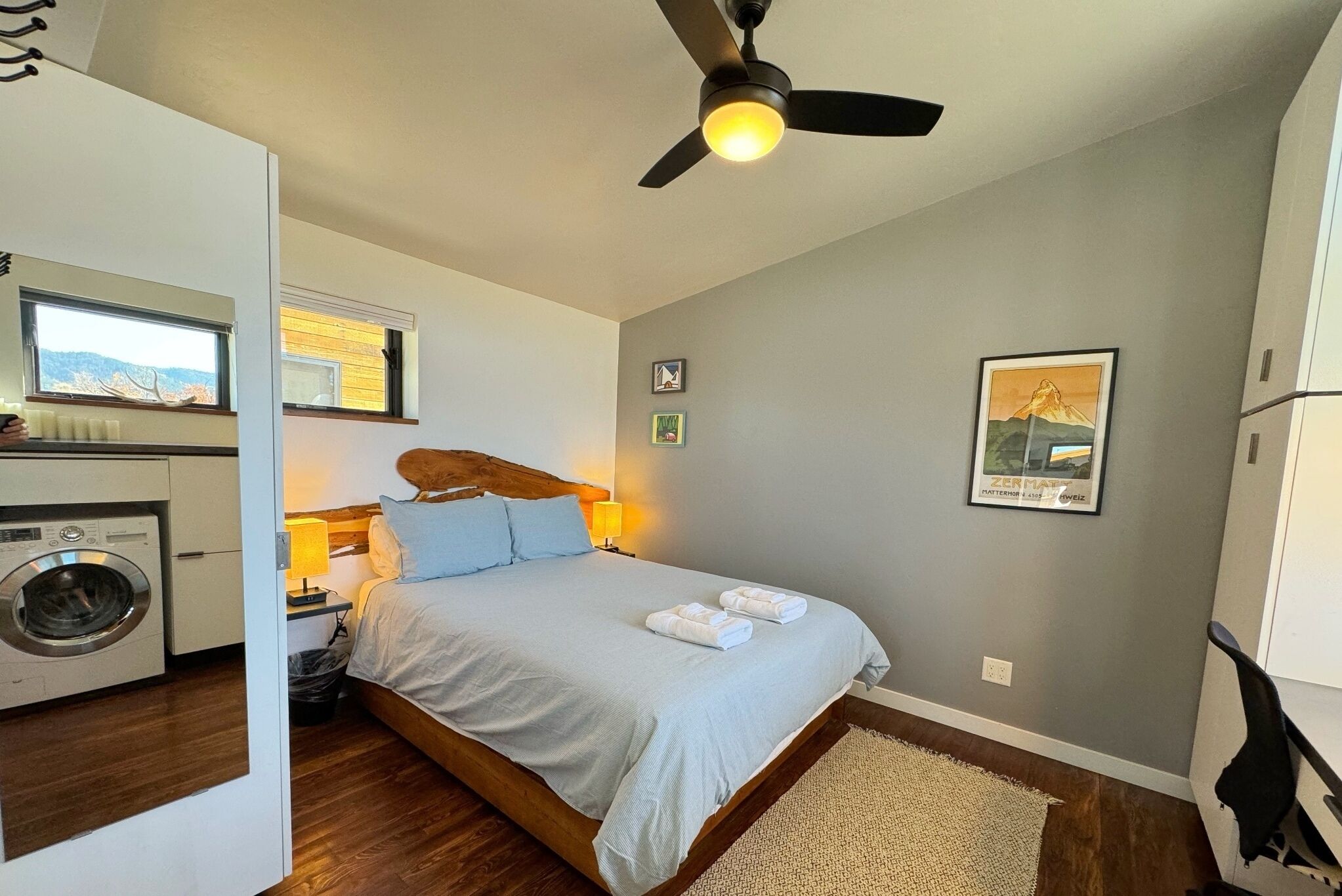 Une chambre avec un lit, un ventilateur de plafond, un lave-linge et une fenêtre donnant sur un beau paysage.