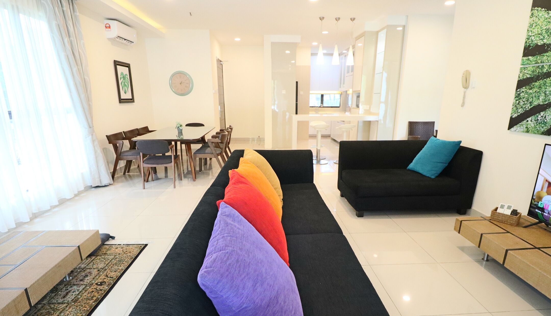 A modern living room with a black sofa, a colorful rug, and a dining area with wooden chairs and a table.