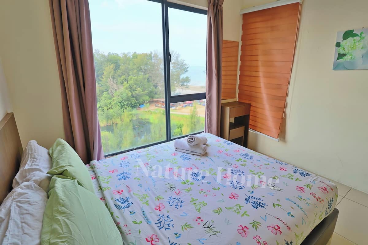 Une chambre à coucher avec un lit, des oreillers, une fenêtre avec des rideaux et une vue sur la verdure et les bâtiments environnants.