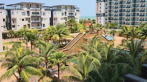 A modern hotel with multiple floors, a swimming area, and palm trees. - Swiss Garden Residences by Nature Home (Balok)