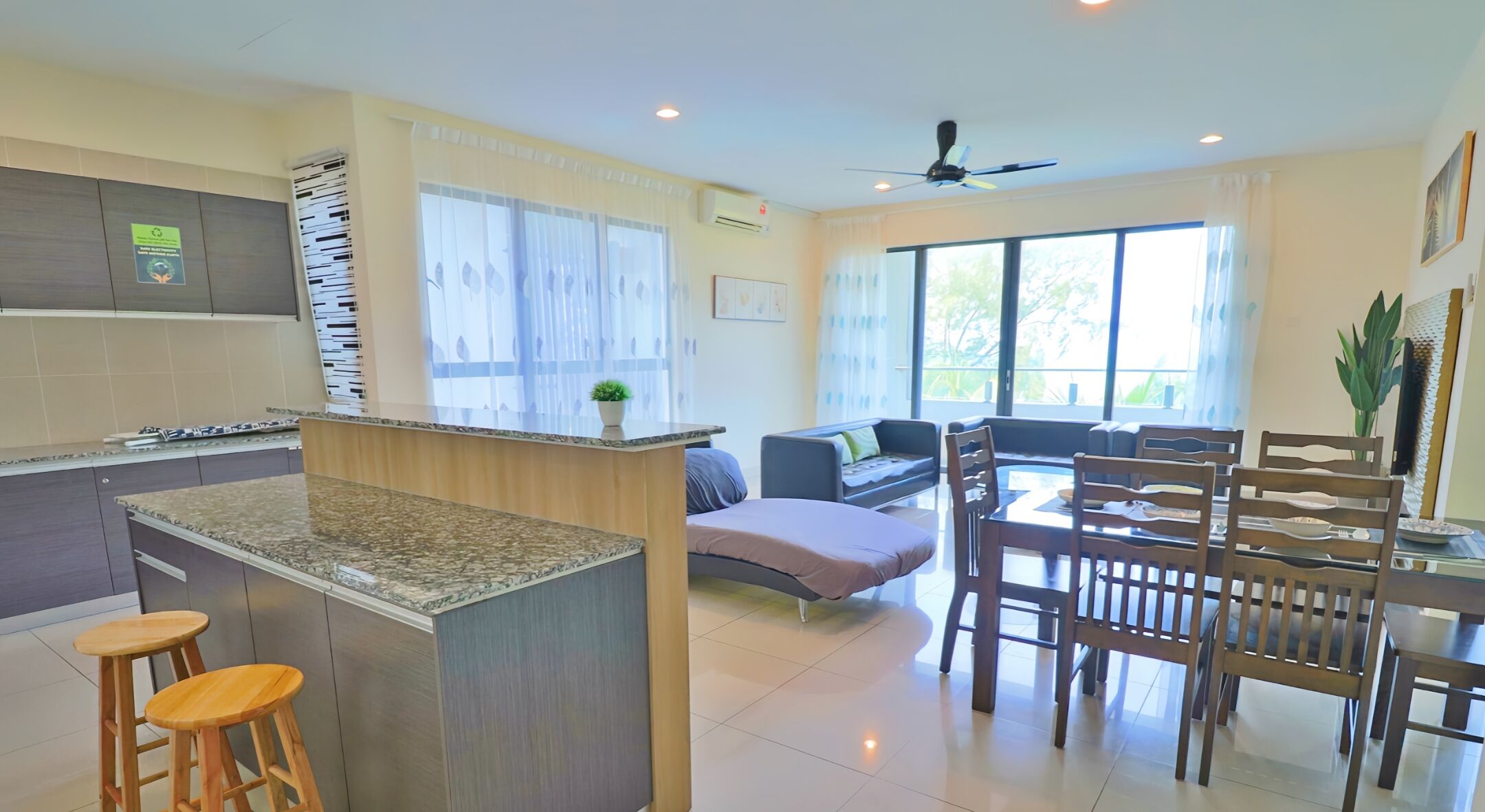 A modern kitchen with a central island, a dining area with wooden chairs, and a living space with a sofa and a coffee table.