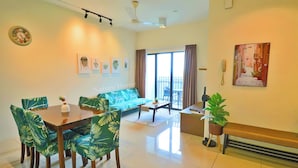 A modern living room with a dining table, chairs, a sofa, a bench, and a balcony with curtains. - Swiss Garden Residences by Nature Home (Balok)