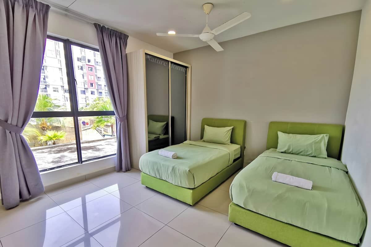 Une chambre d’hôtel avec deux lits verts, un ventilateur de plafond et une grande fenêtre avec des rideaux.