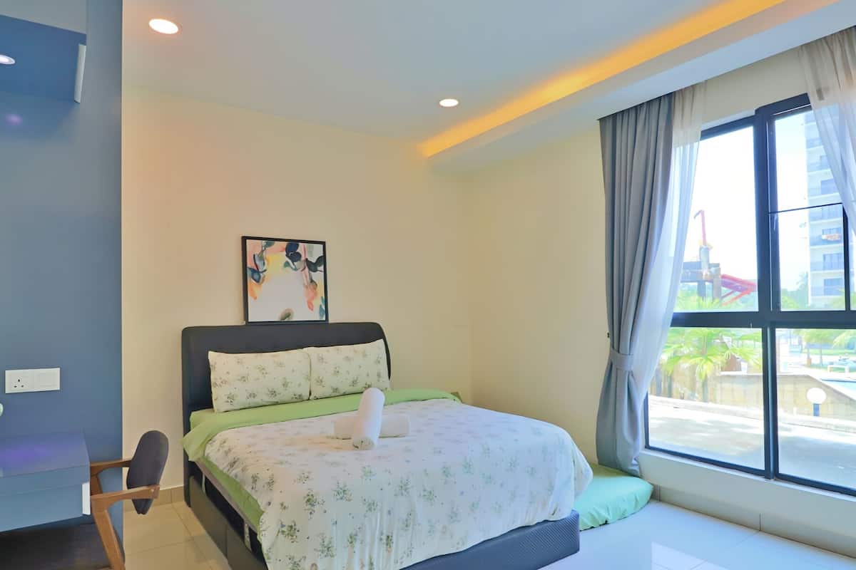 Une chambre moderne avec un lit, un bureau et une fenêtre donnant sur une piscine et des immeubles.