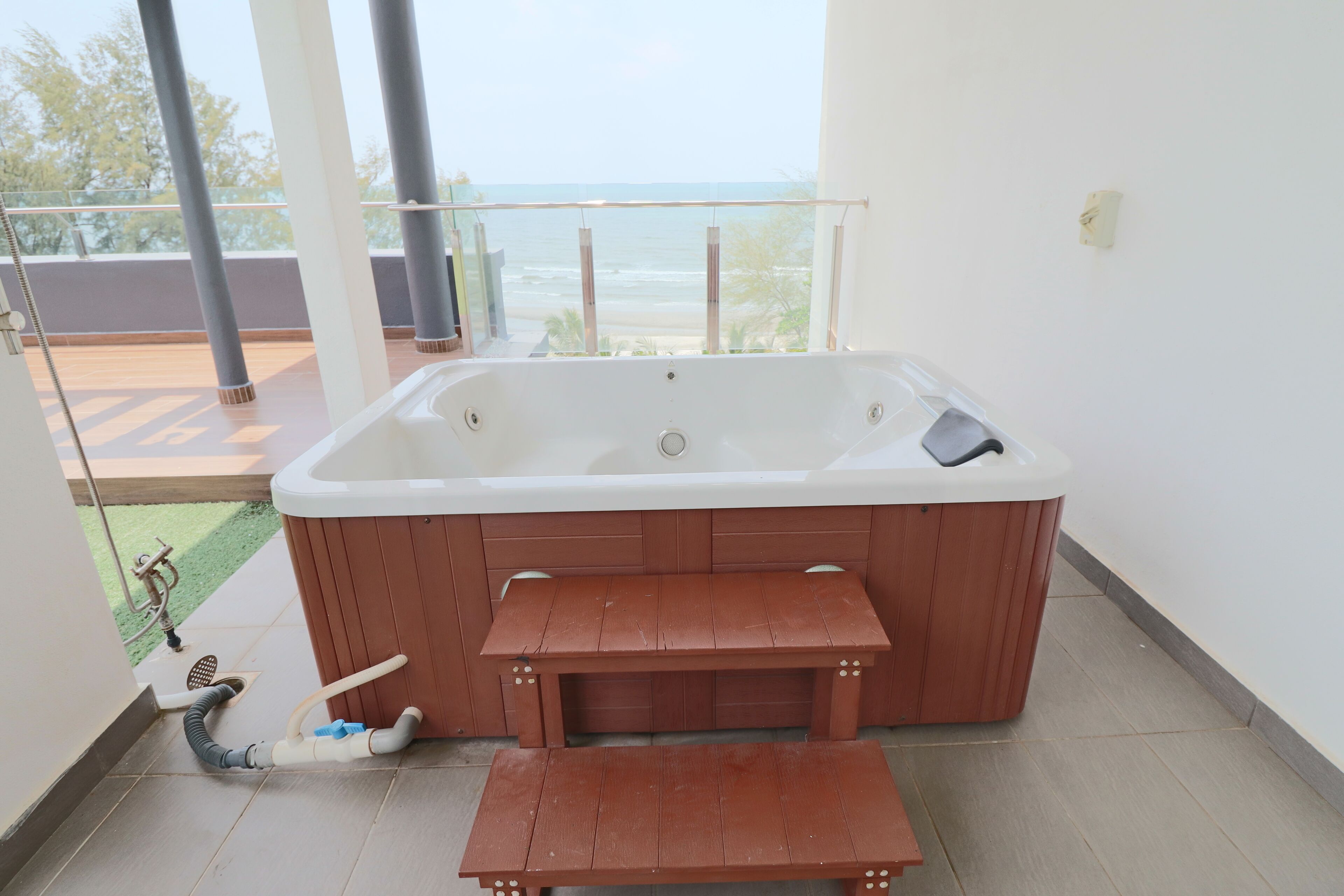 Un jacuzzi con bancos de madera, vista al océano y un balcón con barandilla de vidrio.