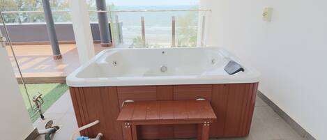 Un jacuzzi con bancos de madera, vista al océano y un balcón con barandilla de vidrio.