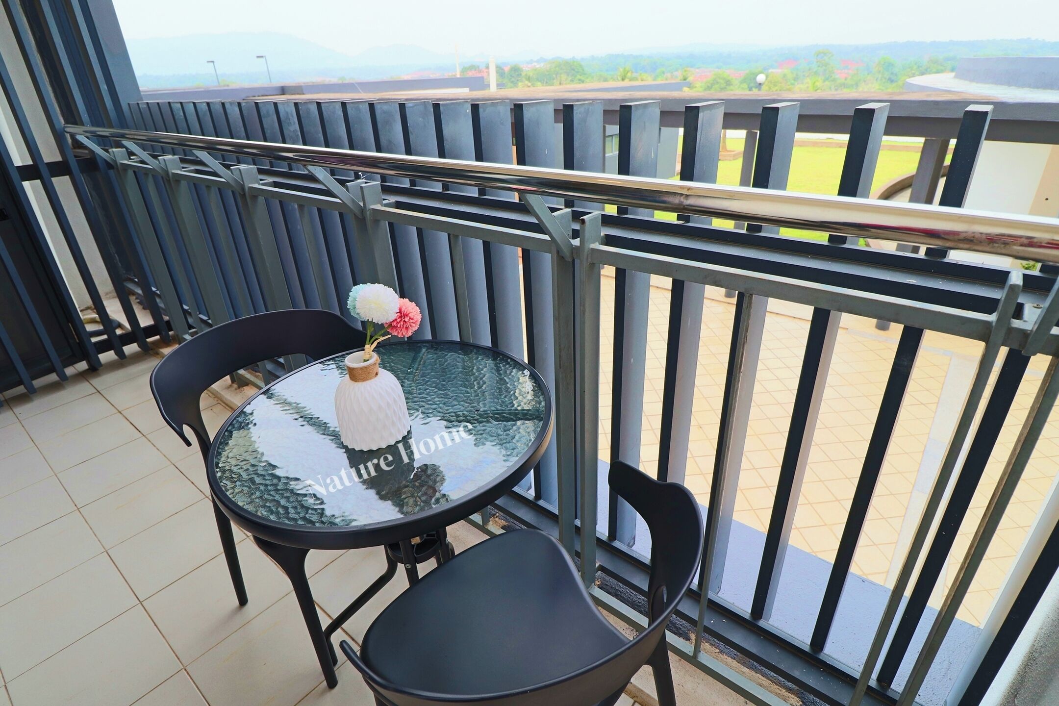 A balcony with a glass table, two chairs, and a vase with flowers.