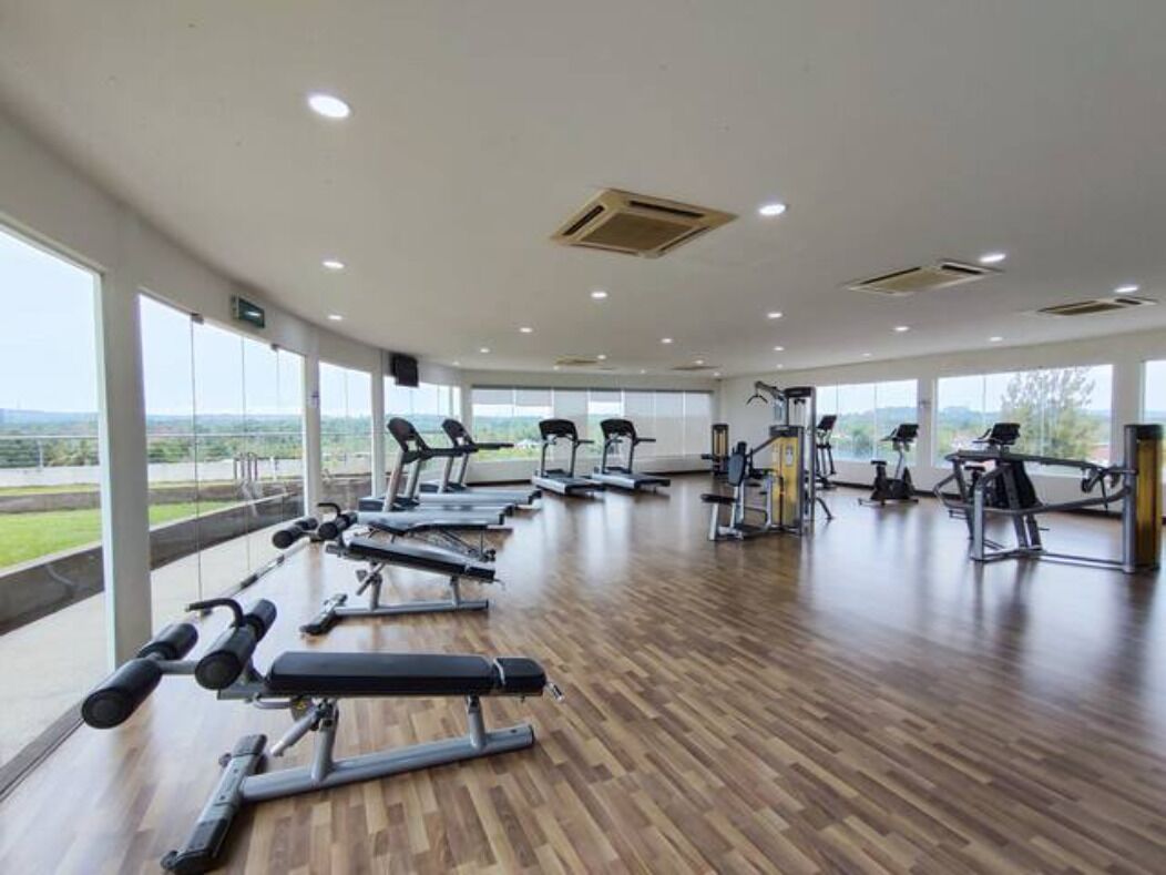 A spacious gym with various exercise equipment, large windows, and a wooden floor.