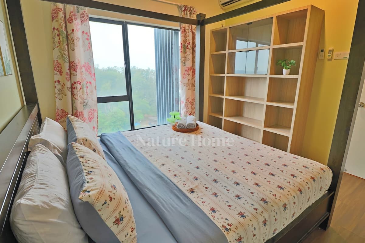 Une chambre avec un lit, des rideaux à motifs floraux, une vue sur la verdure et une bibliothèque intégrée.