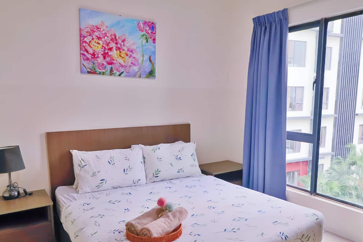 Une chambre d’hôtel avec un lit, une table de chevet, une lampe, un tableau et une fenêtre avec des rideaux.