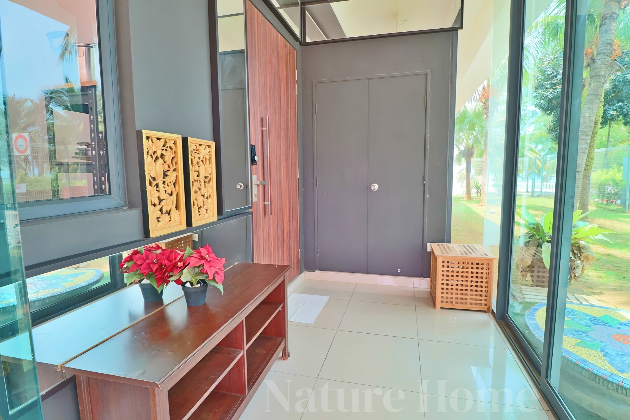 A modern interior with a wooden console table, a grey door, and a view of a garden through large windows.