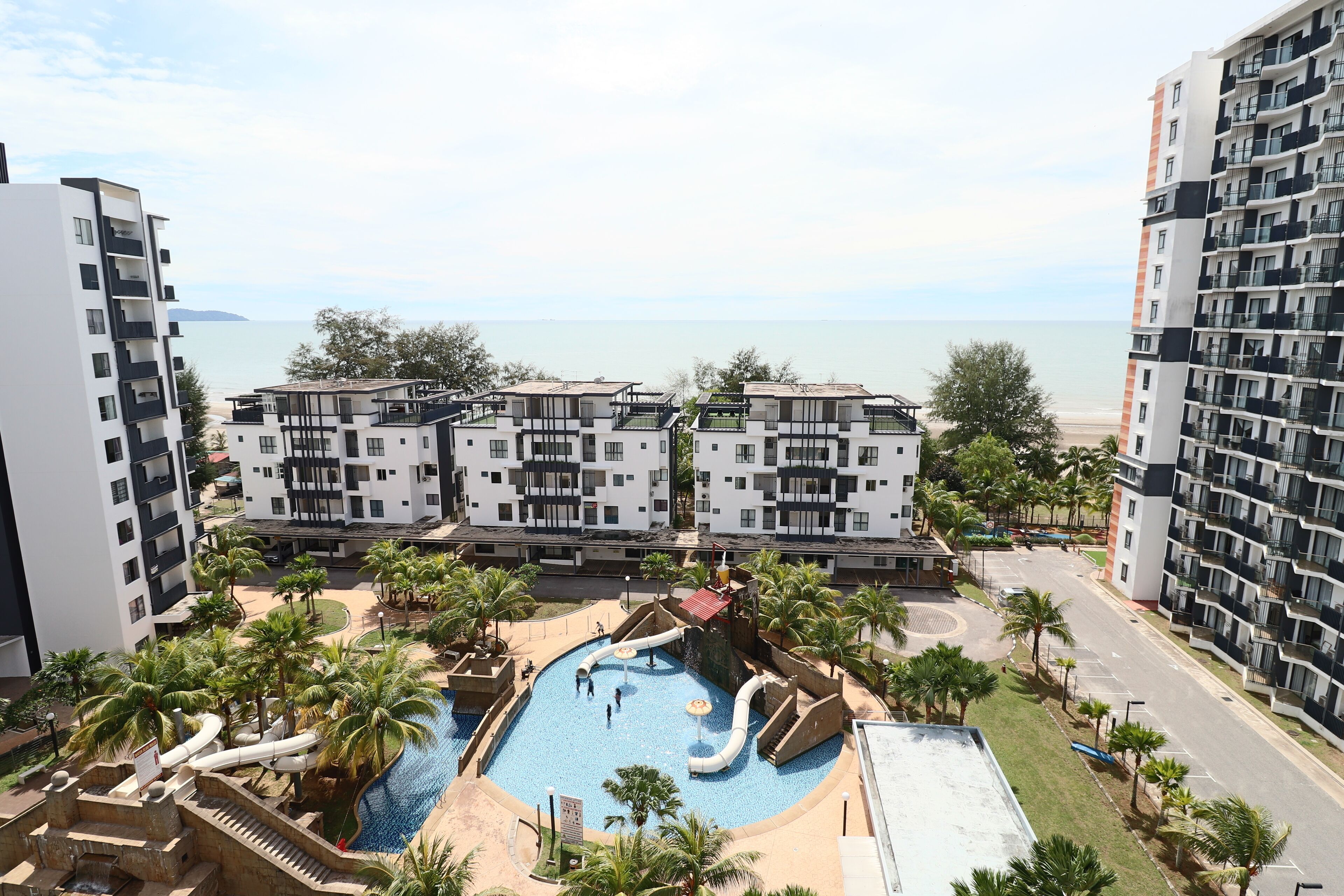 Un hotel moderno con zona de piscina, que incluye toboganes y un tobogán acuático, rodeado de palmeras y vistas al mar.