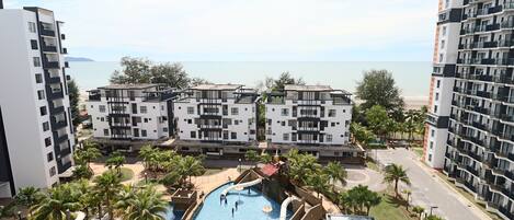 Un hotel moderno con zona de piscina, que incluye toboganes y un tobogán acuático, rodeado de palmeras y vistas al mar.