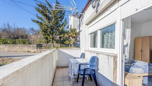 En balkon med et bord, stole, et træskab og et vindue med gardiner.