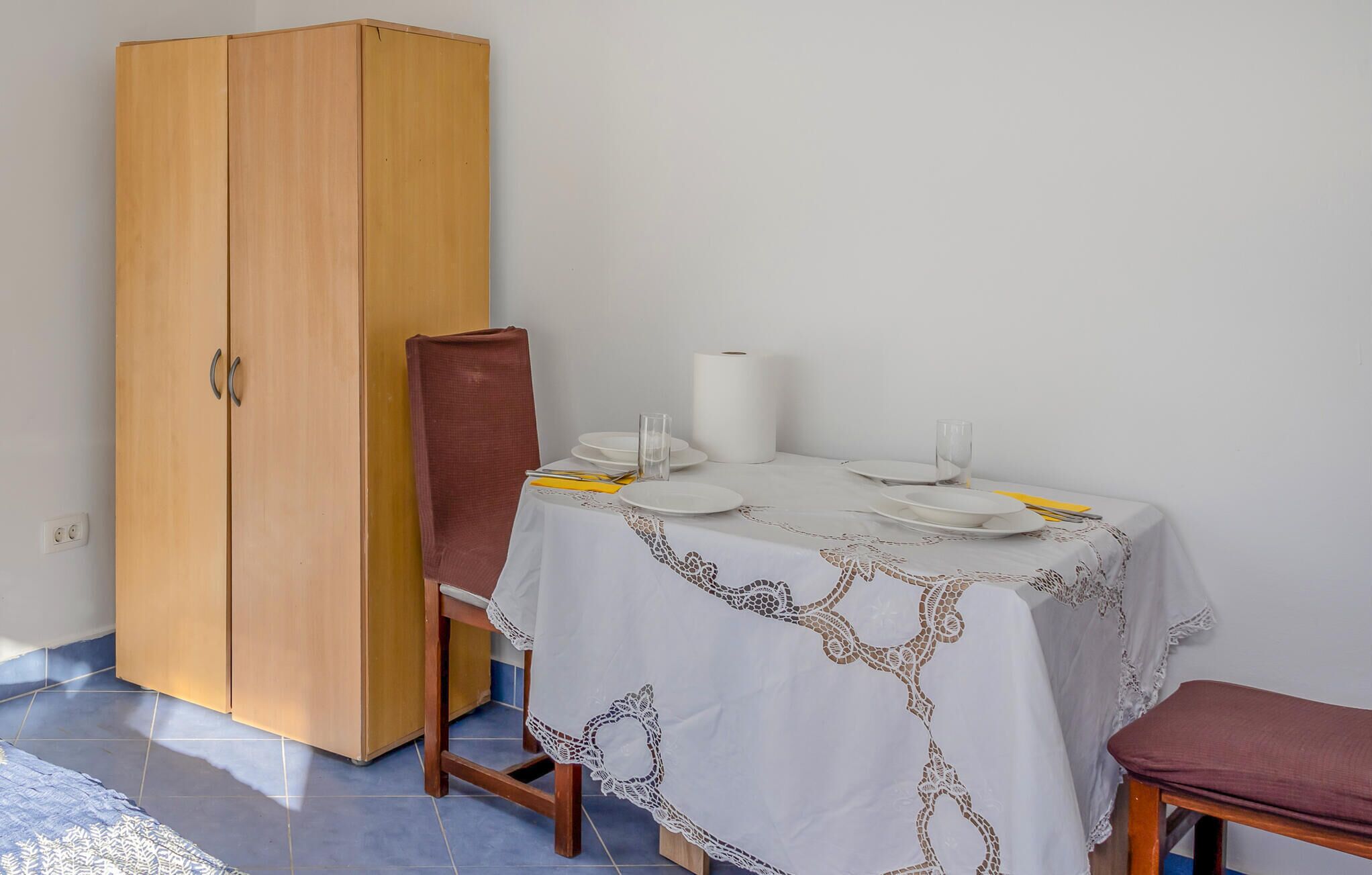 A dining area with a table set for four, a wooden wardrobe, and a chair.