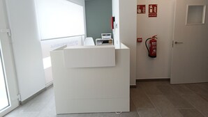 A reception desk in a hotel lobby with a fire extinguisher mounted on the wall and a window providing natural light. - Apartamentos Pontepedriña by Bossh (Santiago de Compostela)