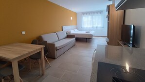 A compact living space with a sofa, a small dining table, a TV, and a window with curtains. - Apartamentos Pontepedriña by Bossh (Santiago de Compostela)