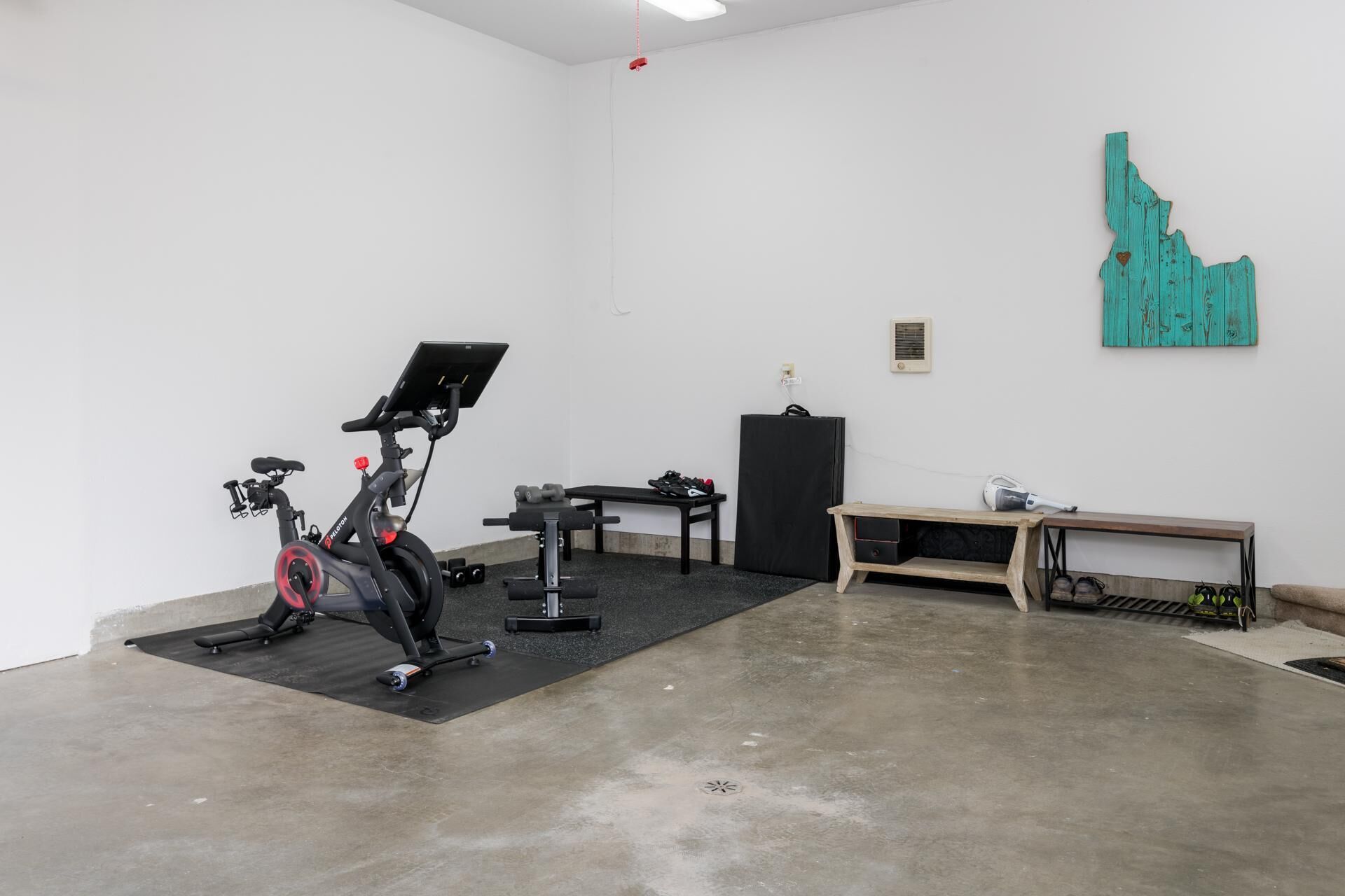 Ein Fitnessraum mit Trainingsgeräten, einer Bank und einem an der Wand befestigten Kunstwerk.