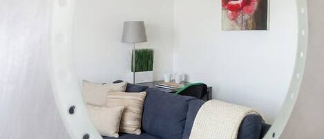 A circular mirror reflecting a living room with a sofa, pillows, a lamp, and a painting.