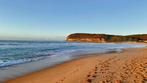 A beach with footprints leading to the water, a clear sky, and a cliff in the background. - Architect design home, walk to Macmasters Beach (MACMASTERS BEACH)