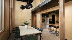 A modern dining area with a wooden table and chairs, a vase with greenery, and a kitchen in the background. - Architect design home, walk to Macmasters Beach (MACMASTERS BEACH)