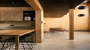 A modern kitchen with wooden cabinets, a wooden dining table, and black chairs. There is a small seating area with a brown sofa and a coffee table. - Architect design home, walk to Macmasters Beach (MACMASTERS BEACH)
