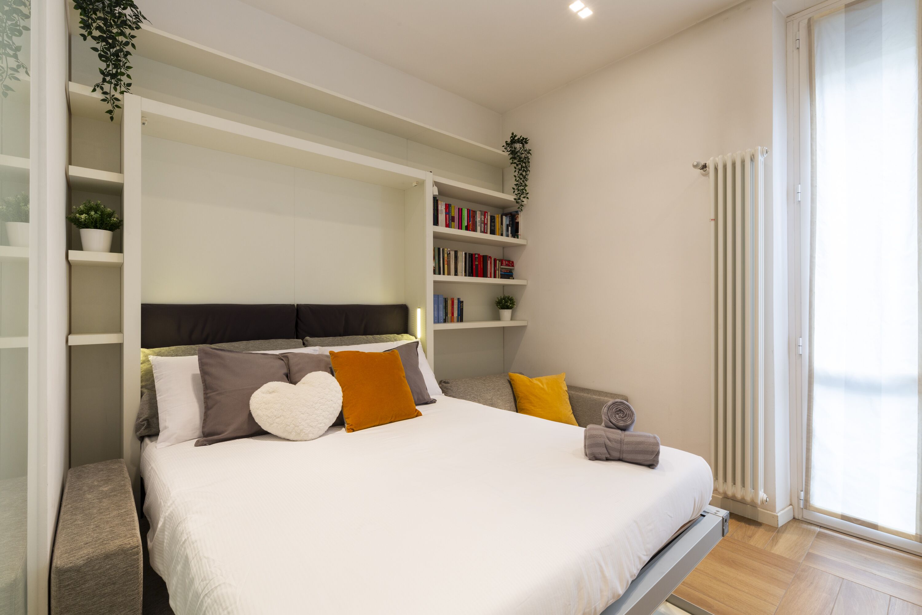 Une chambre à coucher avec un lit, des tables de chevet, une bibliothèque et un radiateur.