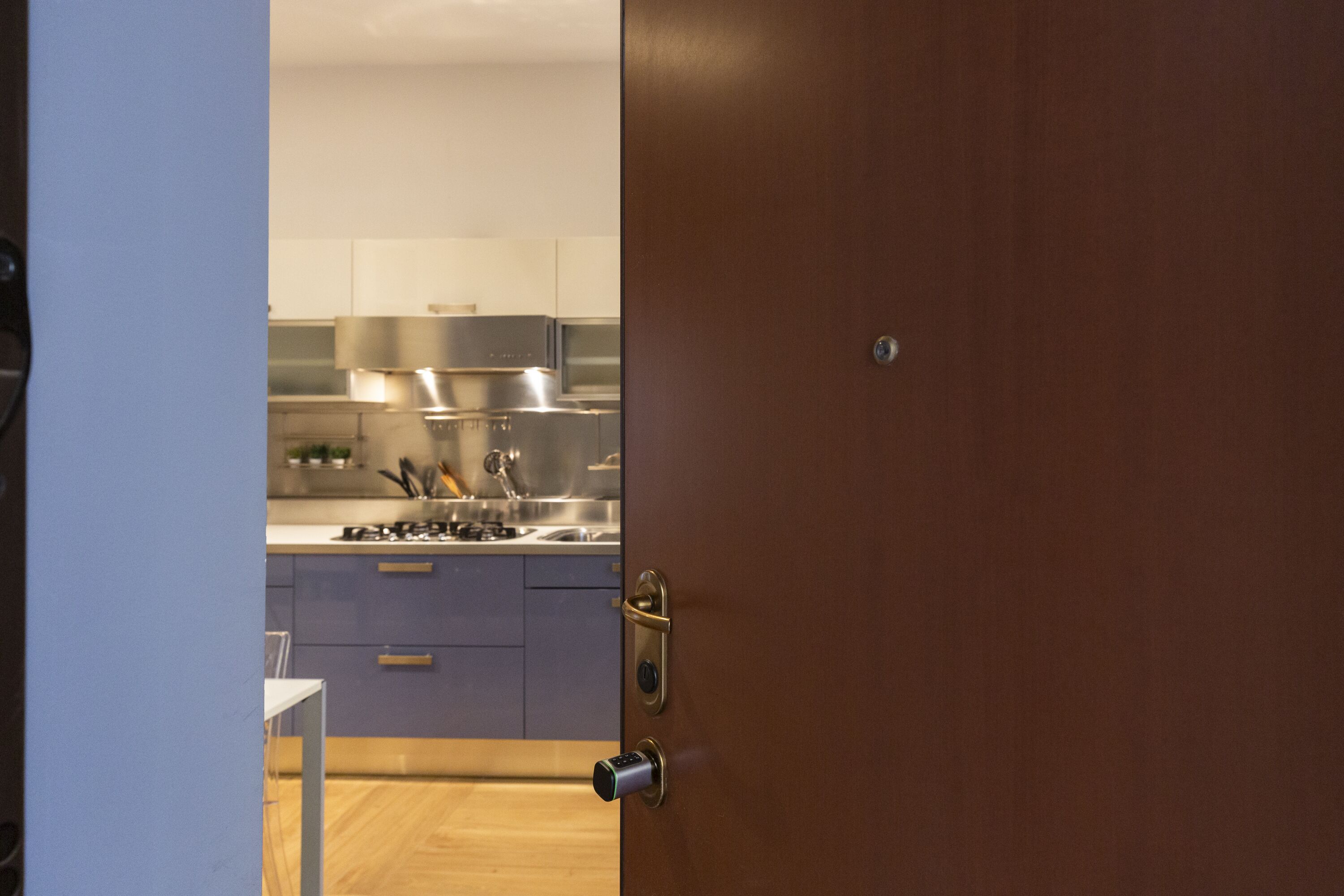 Cozinha moderna com eletrodomésticos de aço inoxidável, piso de madeira e porta com fechadura.