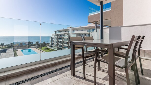 Ein Balkon mit Glasgeländer, der auf einen Pool und ein Wohngebäude blickt.