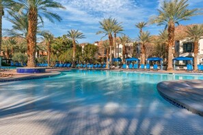 A pool area with blue lounge chairs and palm trees.