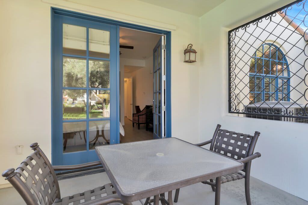 Un patio exterior con una mesa y sillas, una puerta azul y una ventana con reja de metal.
