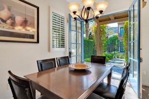 Ein Essbereich mit Holztisch, Stühlen, einer Chandelier und Blick auf einen Garten durch offene Türen.