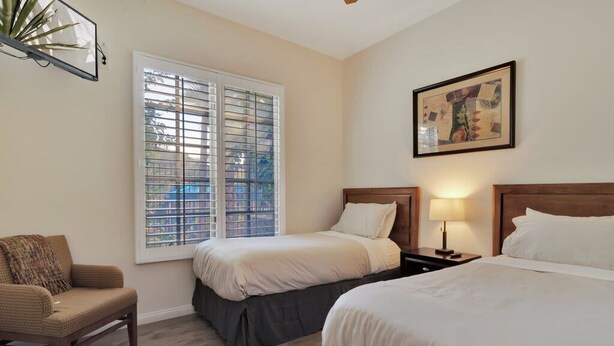 Une chambre d’hôtel avec deux lits, une chaise, une fenêtre avec des stores et un tableau accroché au mur.