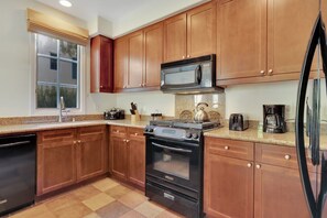 Una cocina con armarios de madera, un microondas de acero inoxidable, una estufa a gas y un refrigerador.
