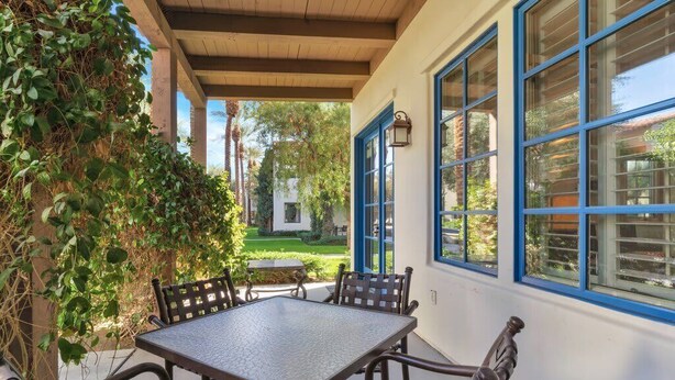 An outdoor patio with a table and chairs, surrounded by a white wall with blue-framed windows.