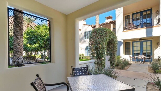 Un patio con una mesa y sillas, vista a un edificio con balcones y un árbol cubierto de plantas trepadoras.