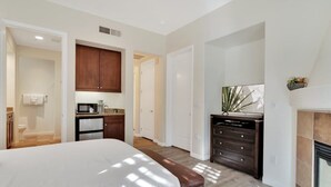 A bedroom with a large bed, a dresser, a microwave, and a fireplace. - Desert Haven C | Studio Legacy Villa (La Quinta)