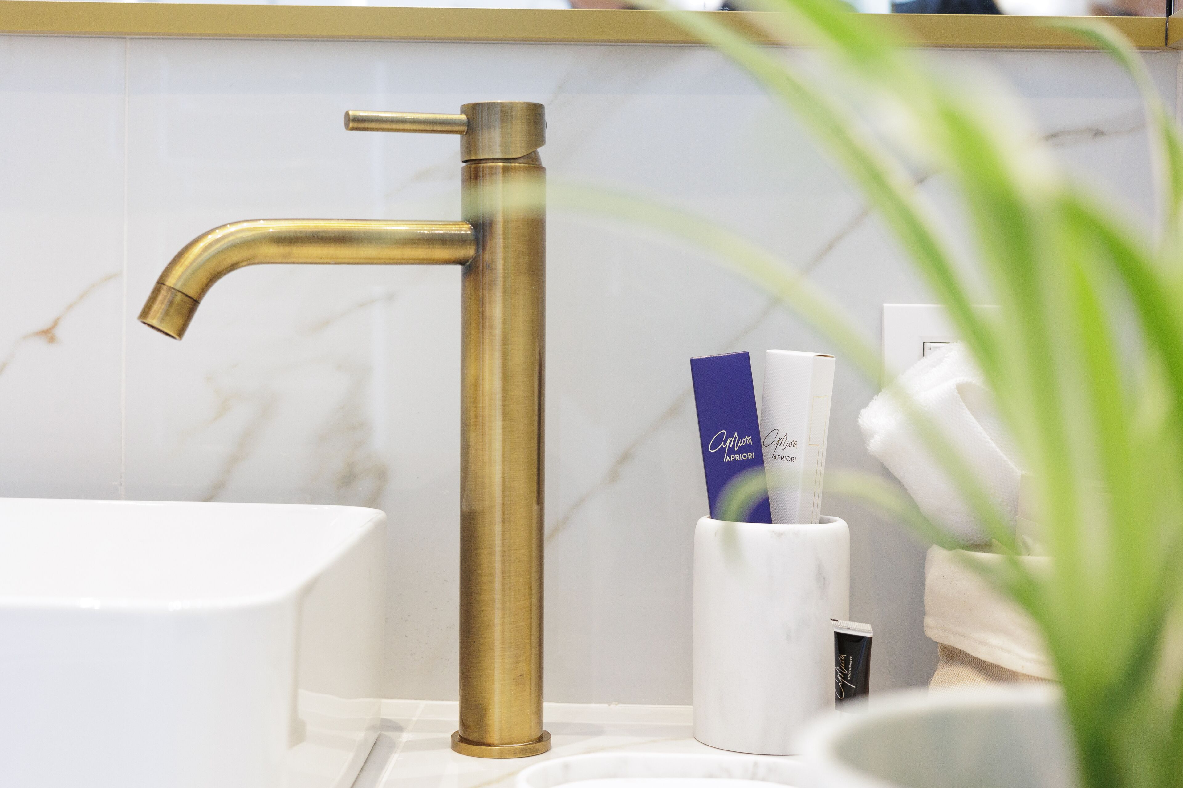 Un baño con grifo dorado, lavamanos blanco y artículos de aseo en un portal blanco.