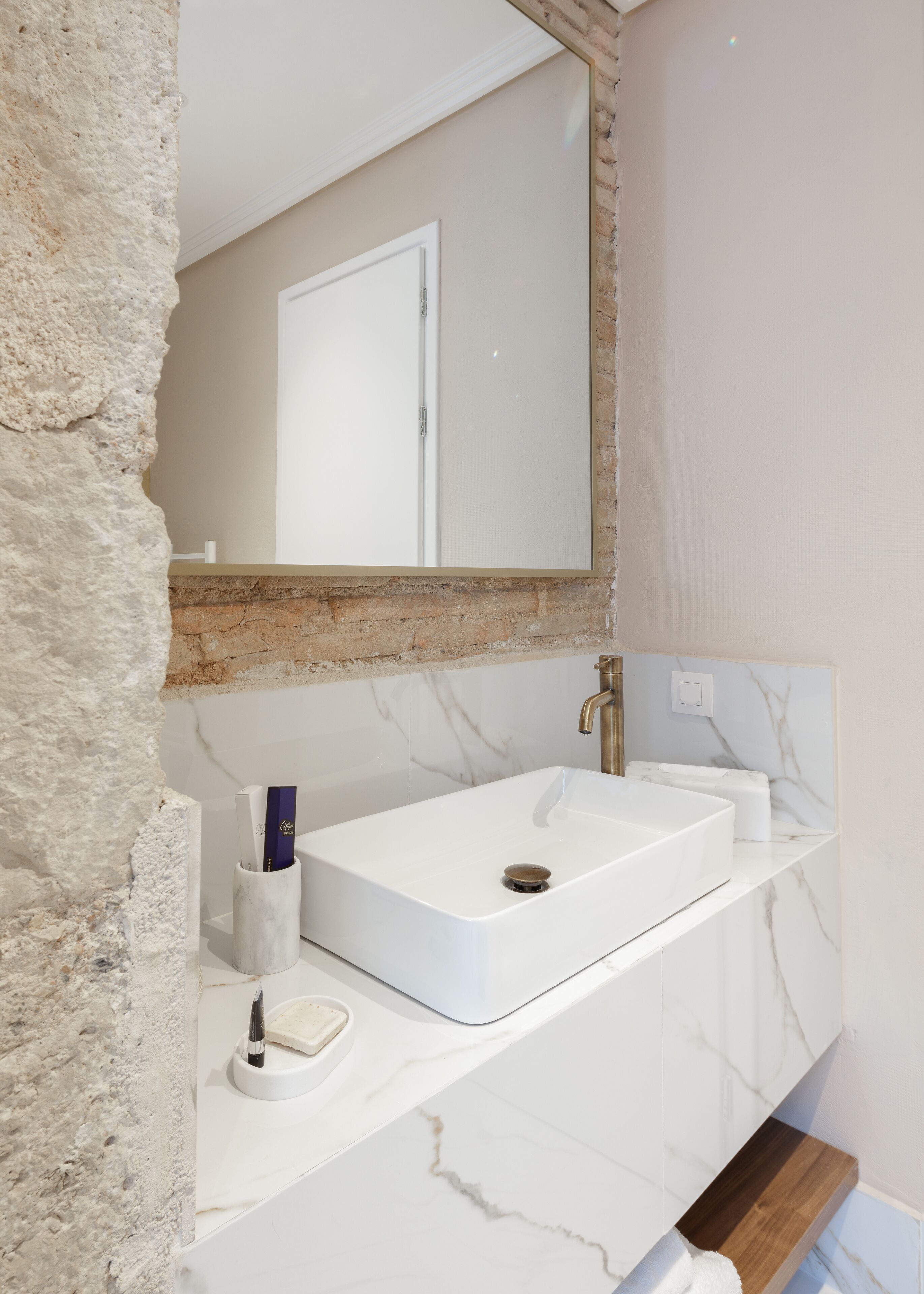 Un baño con lavamanos de mármol blanco, un espejo y una repisa de madera.