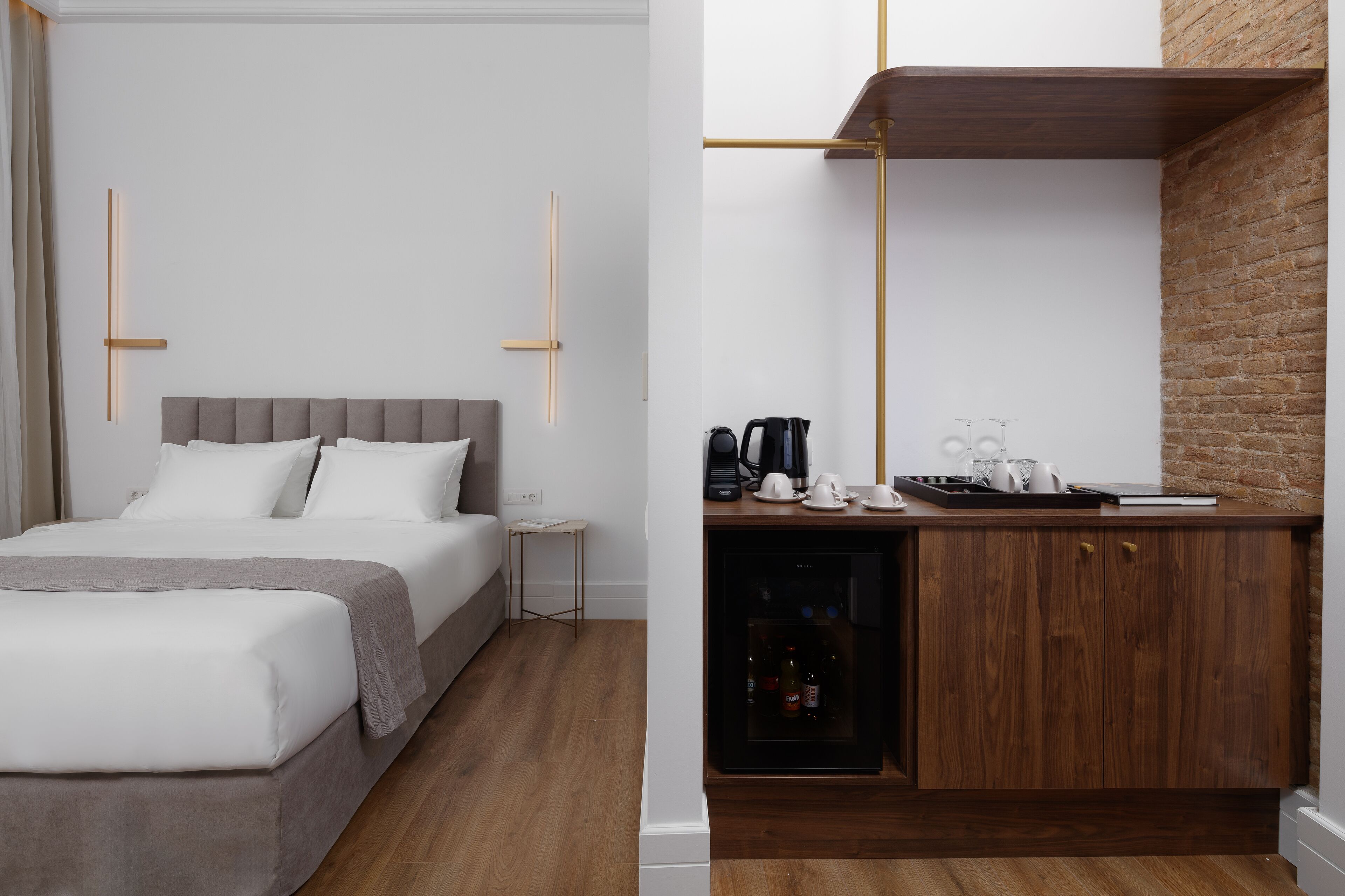 Une chambre d’hôtel moderne équipée d’un lit, d’une table de chevet et d’un coin cuisine intégré avec une machine à café et une bouilloire.