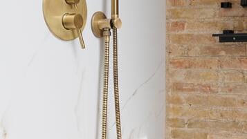 A modern bathroom with a gold showerhead and hose, marble walls, and a brick accent wall.