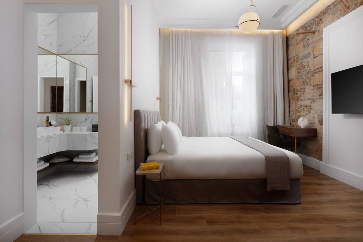 A modern bedroom with a marble bathroom, a large bed, and a stone accent wall.