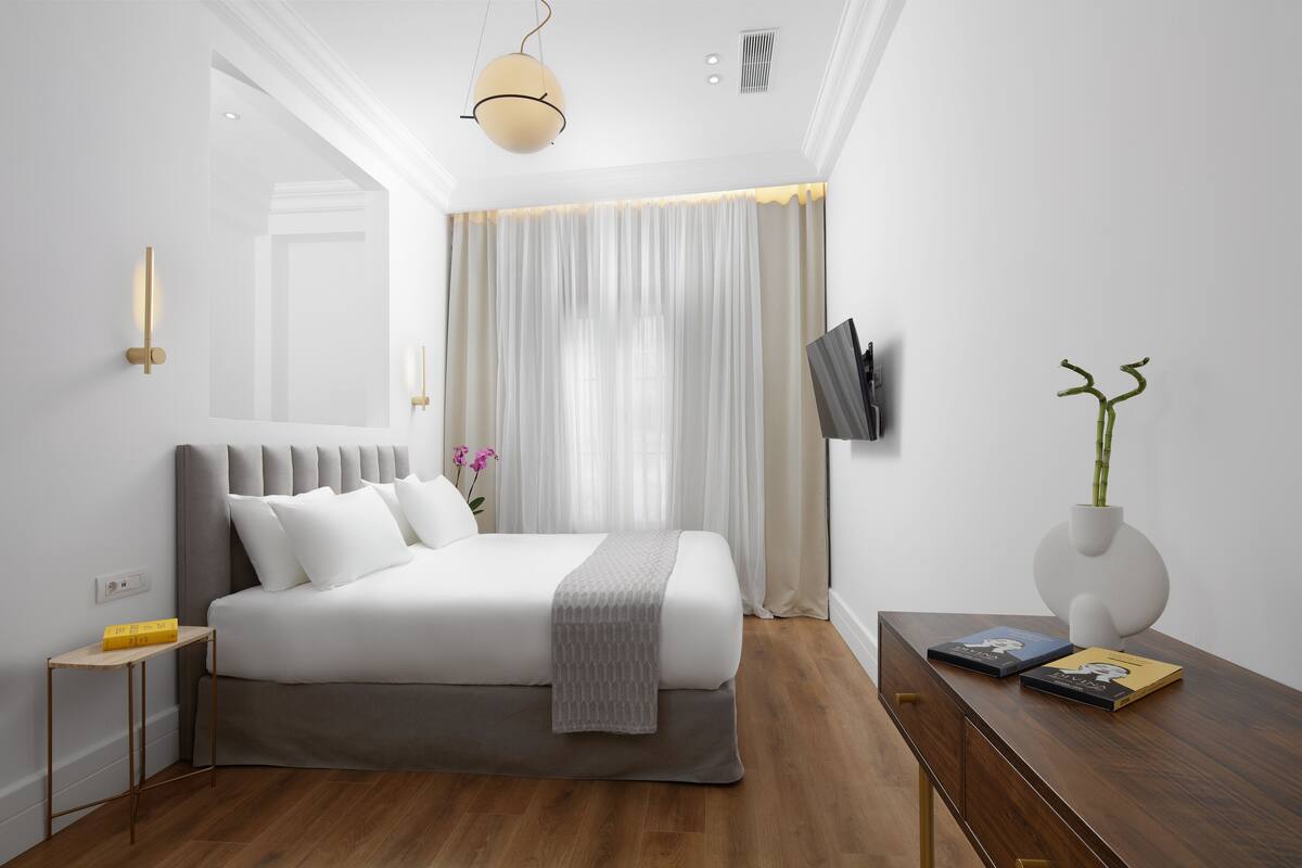 A modern bedroom with a large bed, bedside tables, a bedside lamp, a flat-screen TV, and a decorative vase.
